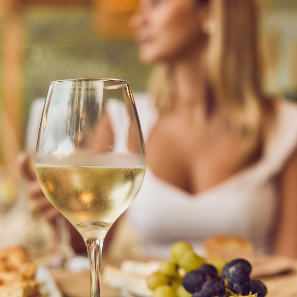 calice di vino in primo piano con ragazza in sfondo che fa degustazione 